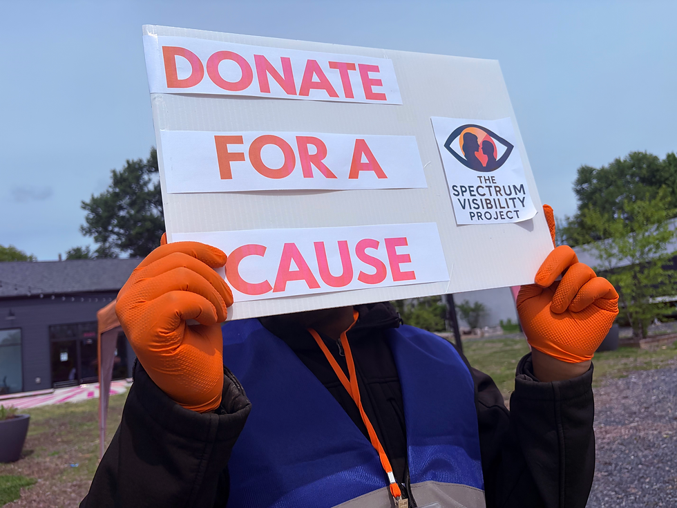 A person with a blue vest and orange gloves holding a "donate for a cause" sign in front of their face.