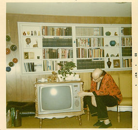 Man poses and tunes in TV set, placed under modern shelving wall, 1968.