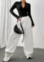 Full shot of woman in black zip-up collared bodysuit, white cargo pants, sneakers, bag, and headphones