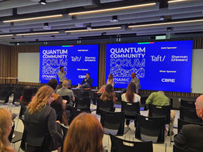Four panelists sit on chairs in front of a bright blue background that says "Quantum Community Forum"
