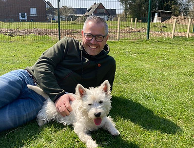 Ein Mann liegt auf dem Rasen und ein weißer kleiner Hund direkt vor ihm.
