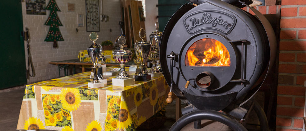 Man sieht einen Ofen, der mit Holz befeuert wird. Er steht in einer rustikalen Diele.