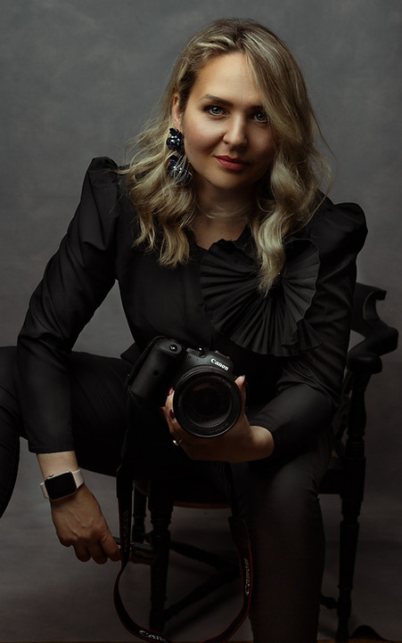Portrait of photographer Vilija Skubute wearing black and holding a Canon camera, seated in studio with a confident and welcoming expression.