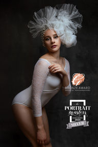 women portrait in white body suit and with white large head piece on her head at vilija skubute photography studio.