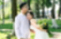 Bride and groom pose smiling beside lush trees.