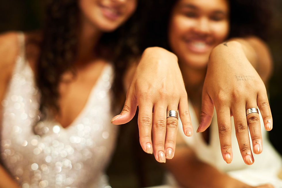 Two brides hold up their hands to show their wedding rings