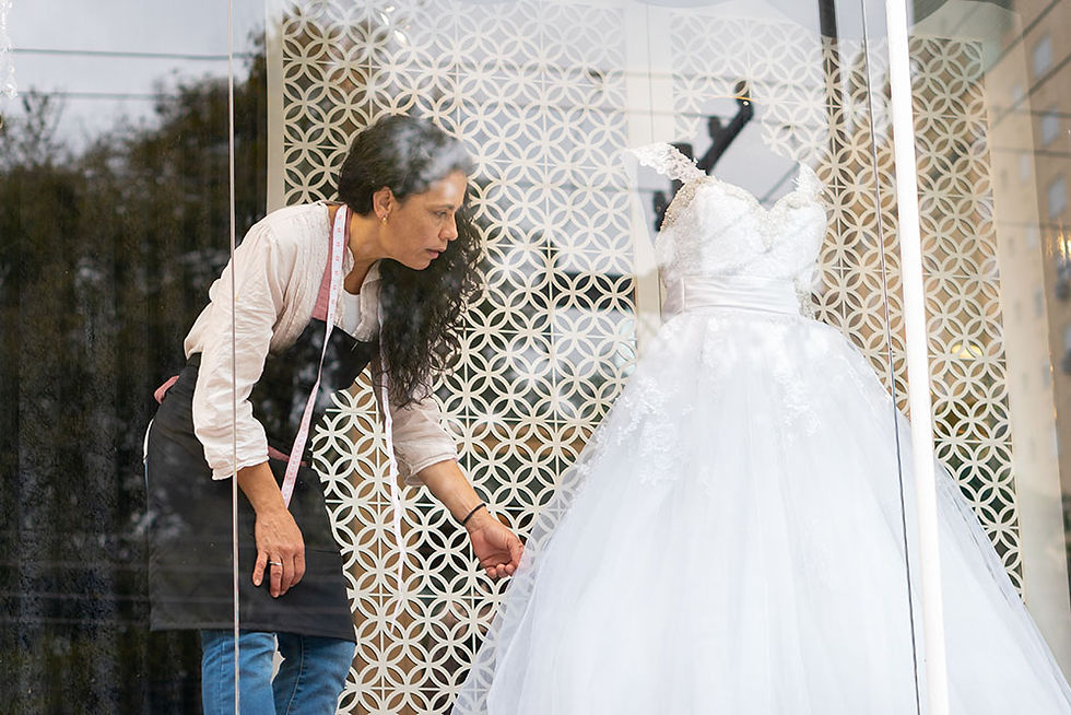 A woman arranges a wedding dress in a storefront window.