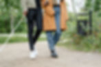 Man with a white cane walks beside his partner in a park, arms linked