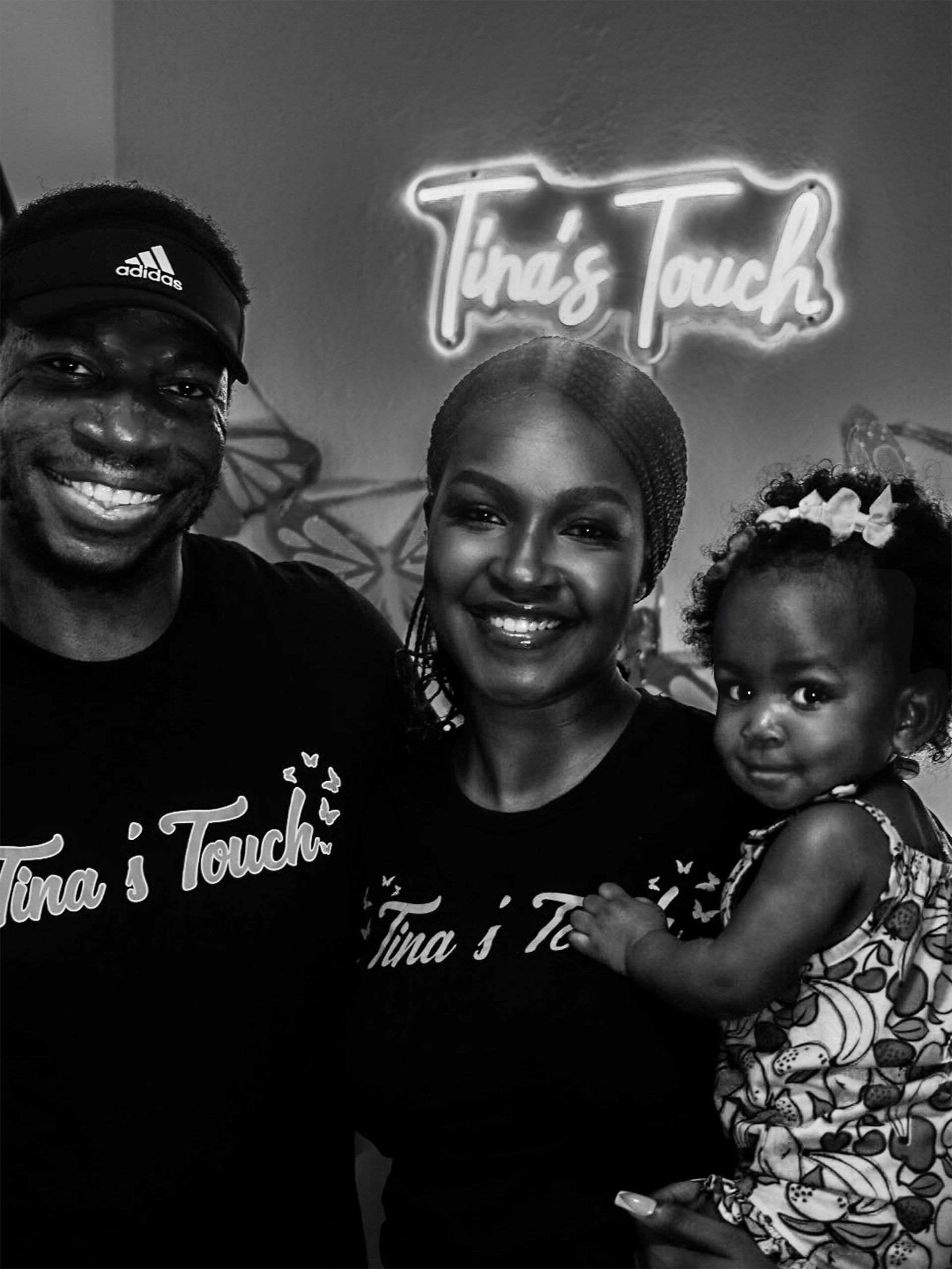 A Family of 3. A woman a Man and a toddler smiling in front of a sign that says Tinas Touch.