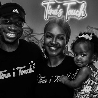 A Family of 3. A woman a Man and a toddler smiling in front of a sign that says Tinas Touch.