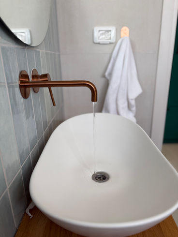 ברז יוצא מהקיר בעיצוב חדר רחצה מודרני, שילוב משטח עץ טבעי ותאורה מיוחדת, רויטל סלמון.