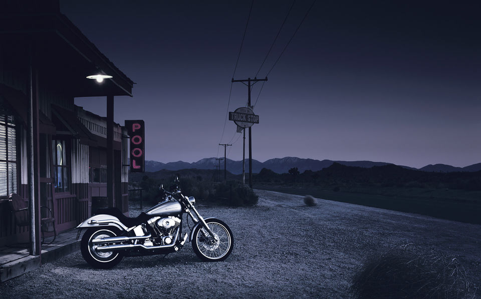A retouched advertising image of a bike parked outside a classic American diner in the desert, at dusk