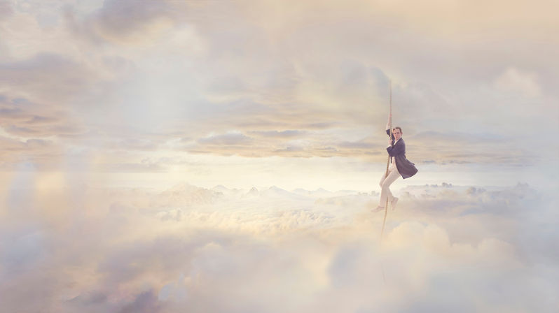 A retouched advertising image of a man in a blazer and white trousers holding onto a rope in an evocative cloud landscape