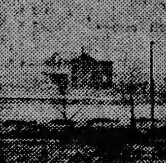 A black and white photo with a grainy texture shows a lone house amidst a barren landscape. A fence and utility poles are visible in the foreground.
