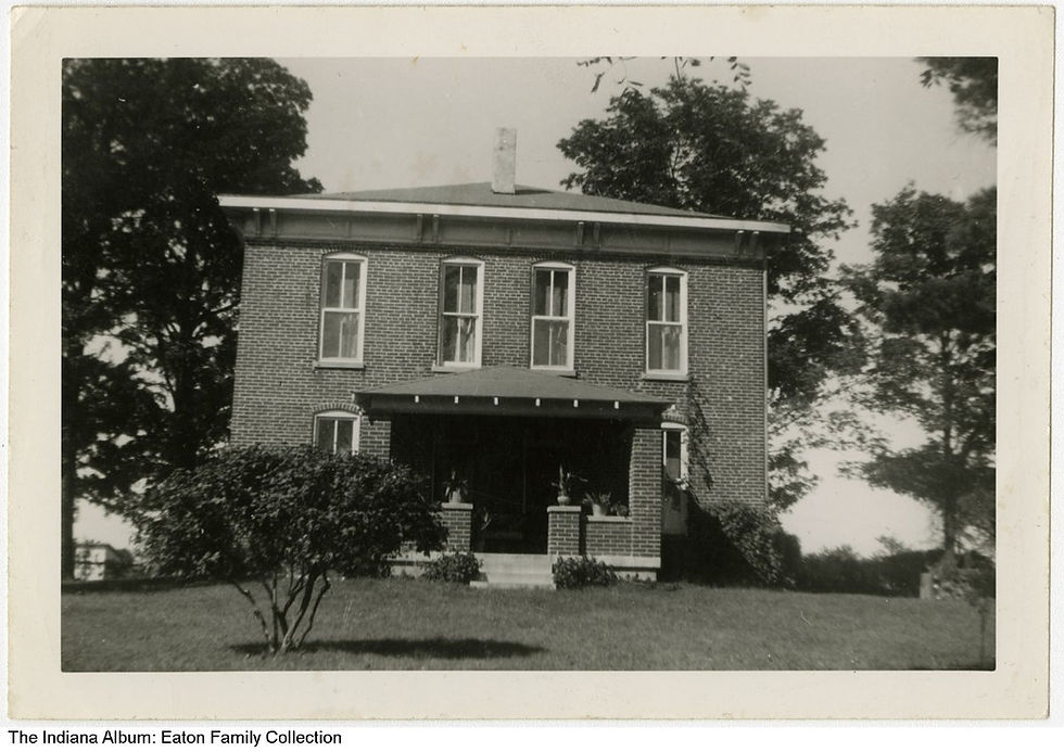 Brick house with many windows and a porch, surrounded by trees. Black and white photo, daytime, calm atmosphere. No visible text.