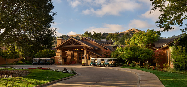 The main entrance of the CordeValle resort with several golf carts parked out front. The building has a large wooden archway, and the surrounding landscape is well-manicured with trees and green grass.