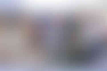 An outdoor vendor booth selling jars of jam and other homemade goods. A woman in a light blue sundress is reaching up to arrange a jar on a multi-tiered display.