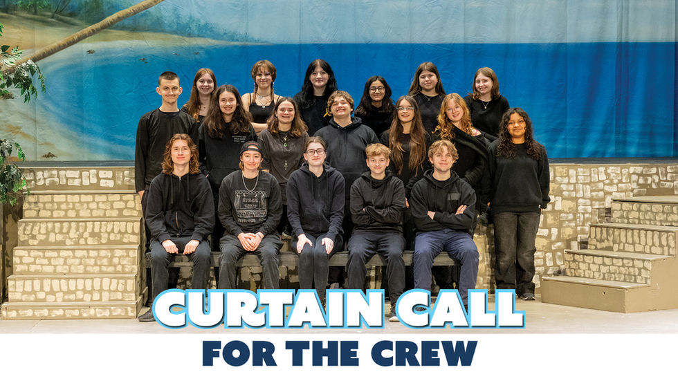 A wide-angle photograph of the entire stage crew posing for a curtain call on a stage. They are arranged in three rows: a seated front row, a standing middle row, and a standing back row. All members wear black clothing, with some in hoodies and others in plain shirts. They are positioned in front of a stage backdrop depicting a beach scene with a blue sea and sky, with some artificial palm fronds visible on the left. To the front and sides are stage blocks painted to resemble stone walls and stairs. At the bottom of the image, there is a white overlay box containing large, stylized blue text that reads "CURTAIN CALL" above smaller dark blue text that reads "FOR THE CREW".