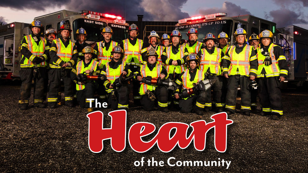 A group of approximately 20 firefighters from the Fuller Hose Volunteer Fire Department posing in full turnout gear and high-visibility vests. They are positioned in front of two gray fire trucks with their emergency lights flashing under a dramatic, cloudy twilight sky. Several firefighters in the front row are kneeling and holding hydraulic rescue tools.