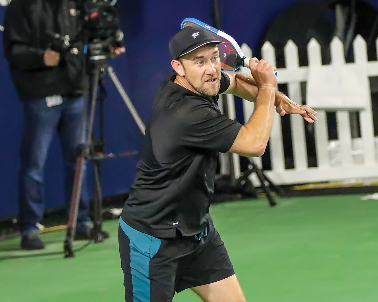 Professional pickleball player Patrick Kawka, wearing a black shirt and hat, hits a forehand drive shot from the baseline during the Pro Men's Singles finals match against Ronan Camron.