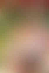 A father stands next to his young daughter who is riding a horse on a brightly lit carousel at the festival carnival.