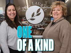 Christina Moore and Marsha Bauer, founders of The Laurel Marketplace, standing in front of their shop’s glass entrance in downtown Greensburg. The door features the marketplace logo and posted business hours.