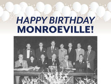 A celebratory graphic with a cream to light grey gradient background. At the top, there is a decorative border of various white balloons with strings. Centered below the balloons is the text "HAPPY BIRTHDAY MONROEVILLE!" in bold, dark blue capital letters, arranged on two lines. Below the text is a faded, black and white group photograph showing 13 people, mostly men in suits and one woman, seated and standing behind a long table with large floral arrangements.