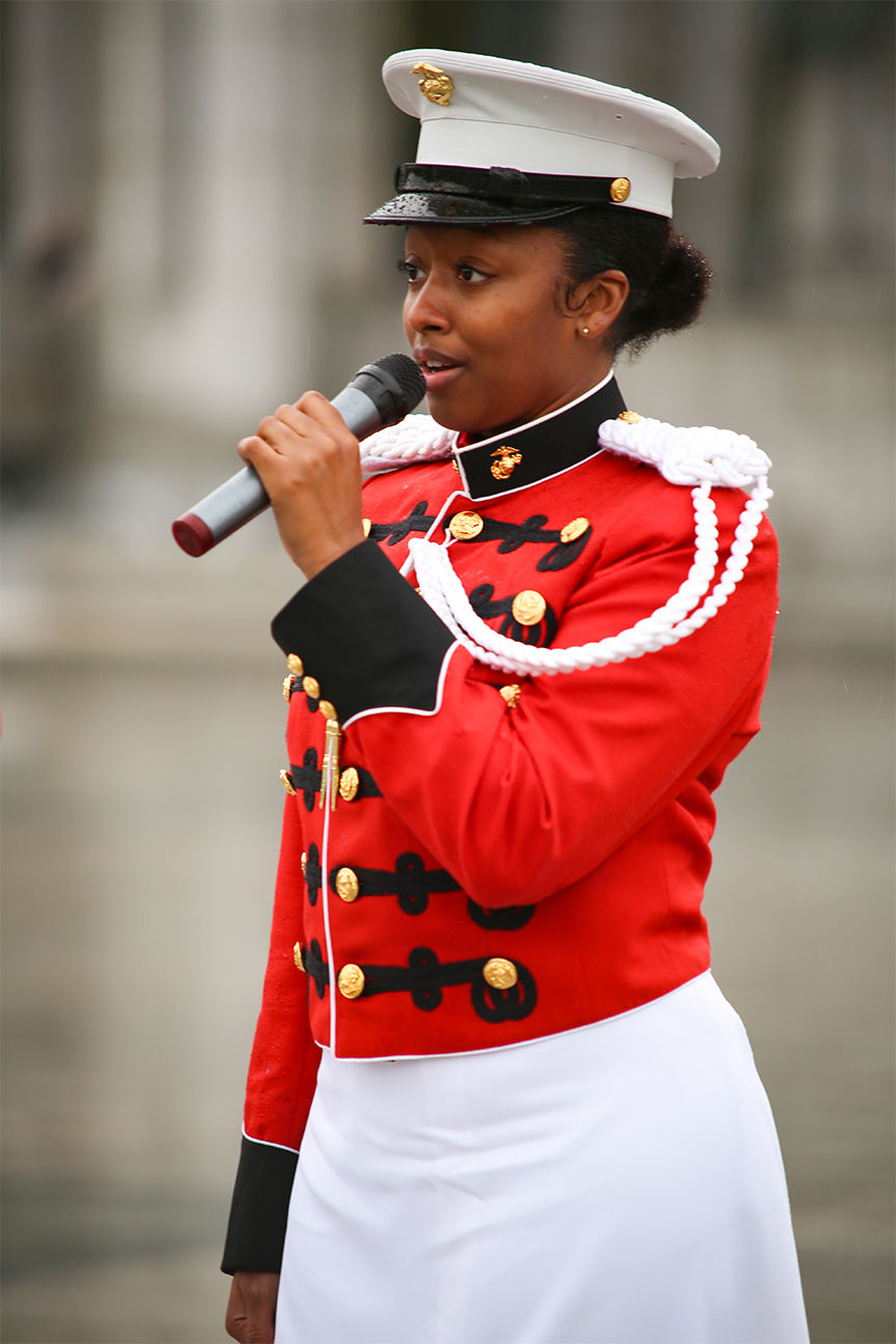 Marine Staff Sgt. Hannah Davis in her official dress uniform singing into a microphone while performing on stage.