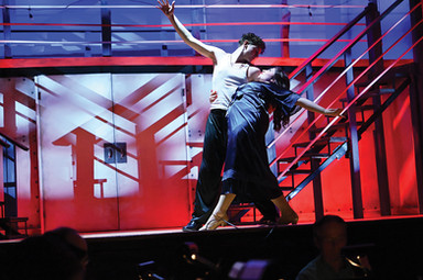 A man and woman are dancing on stage, with the woman wearing a black dress.