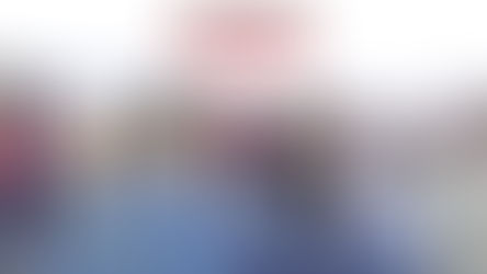 A group of children playing pickleball games outdoors on a blue court, with a coach in a cowboy hat watching. Yellow and orange circles are painted on the court surface for a fun, youth-focused drill.