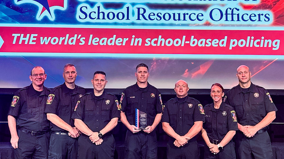 A photograph taken during an award ceremony on an auditorium stage. The background features a large screen with a glowing blue and white banner at the top reading "Association of School Resource Officers". Below it, a large red banner has white text reading "THE world's leader in school-based policing". Six uniformed Peters Township School Resource Officers, the same group from the feature image, stand in a line across the stage, facing the camera. The officer in the center holds a rectangular glass award plaque. They are on a dark stage with black curtains behind them.