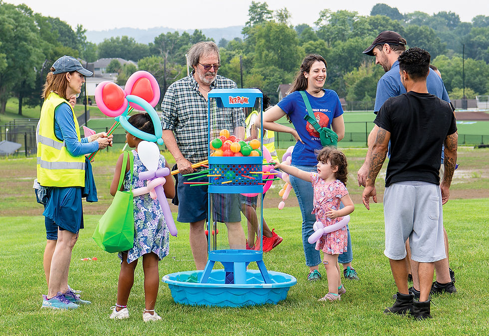 Children and adults gather around a giant KerPlunk game set up on a grassy field during the community day event.