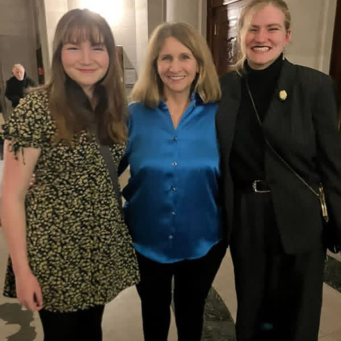 Soph (right) stands smiling next to her voice teacher Betsy Lawrence (middle) and her sister Phoebe (left) in an indoor setting.