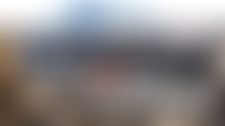 An indoor pickleball court with two players on it. The facility has high ceilings, a lounge area with tables and chairs, and large banners on the walls with images of pickleball players.