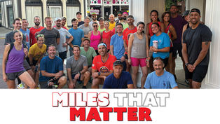 A group of approximately 30 runners from the Sewickley Runners Club posing together on a street corner in front of a white building. The members are dressed in colorful athletic wear, with some standing and others kneeling, capturing the community spirit of their weekly Tuesday evening meet-up.