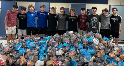A group of male teenagers stands behind a massive pile of donated bags of food.