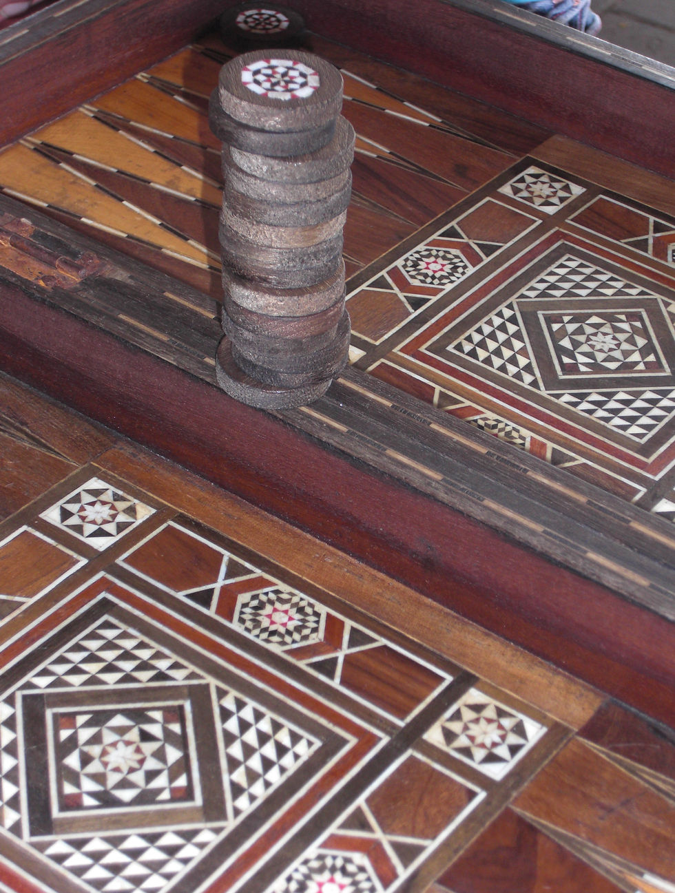 A close-up photo of a wooden backgammon board with decorative geometric inlays and a stack of brown checkers. I didn’t ask about their favorite games, but in Tel Aviv, Shesh Besh is the winner. It’s a secular ritual—a mosaic of history played out on a board.
