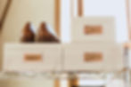 Brown shoes sit on a labeled box alongside two other labeled boxes on a wire shelf in a sunlit room, creating an organized, warm atmosphere.