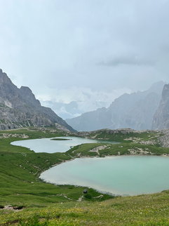 blauer See mit grünen Wiesen und Bergen im Hintergrund, Dolomiten
