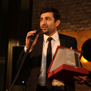 Man in suit speaking at microphone holding an award.