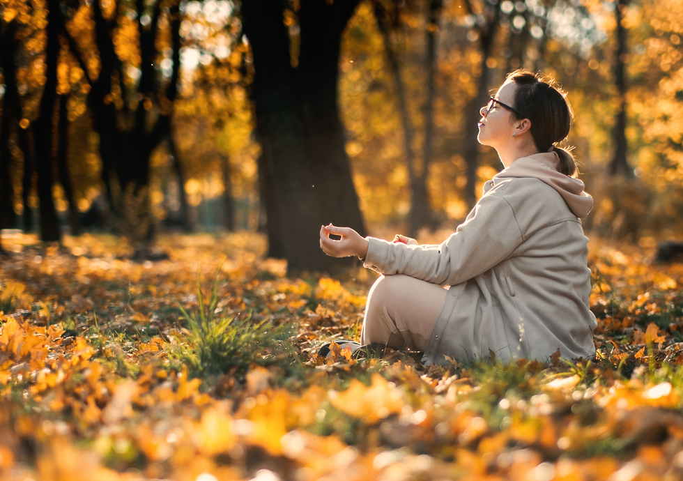 eine Frau sitzt in entspannter Yogahaltung im Herbstwald und tankt Energie