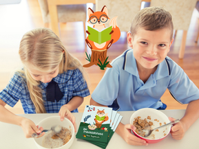 ein Mädchen und ein Bub sitzen nebeneinander am Tisch und frühstücken ein Müsli, der Bub schaut in die Kamera, mit Logo vom Frühstücksfuchs und Frühstücksfuchs-Tagebüchern am Tisch.