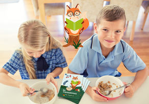 ein Mädchen und ein Bub sitzen nebeneinander am Tisch und frühstücken ein Müsli, der Bub schaut in die Kamera, mit Logo vom Frühstücksfuchs und Frühstücksfuchs-Tagebüchern am Tisch.
