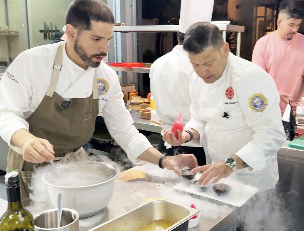 Chef Irvin Van Oordt and Chef Arjun Ranabhat in a kitchen are focused on preparing a dish with dry ice, creating smoke. A third person in pink stands in the background. Molecular Gastronomy Masterclass by Chef Nepal