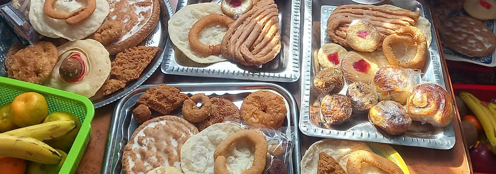 Assorted breads and pastries on trays with bananas and tomatoes in baskets. Sunlight casts shadows, creating a warm and inviting scene.