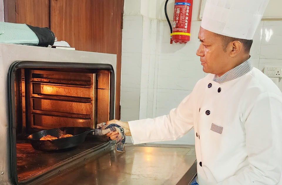 Chef Suresh Prajapati pulls a skillet from a glowing oven in a kitchen, focused on cooking.