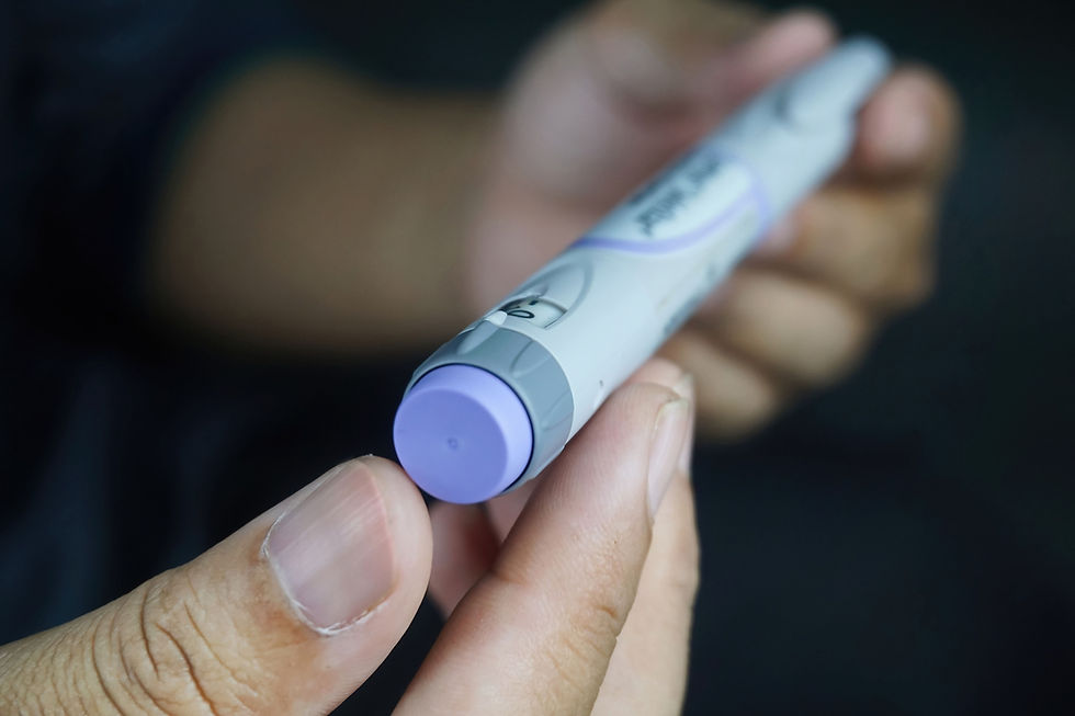 Close-up of a hand holding a lavender-and-white insulin pen, with blurred fingers in the background against a dark backdrop.