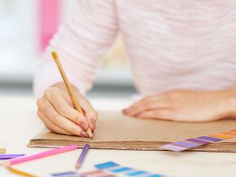Une main tient un crayon pour écrire sur la page d'un cahier ouvert sur une table.