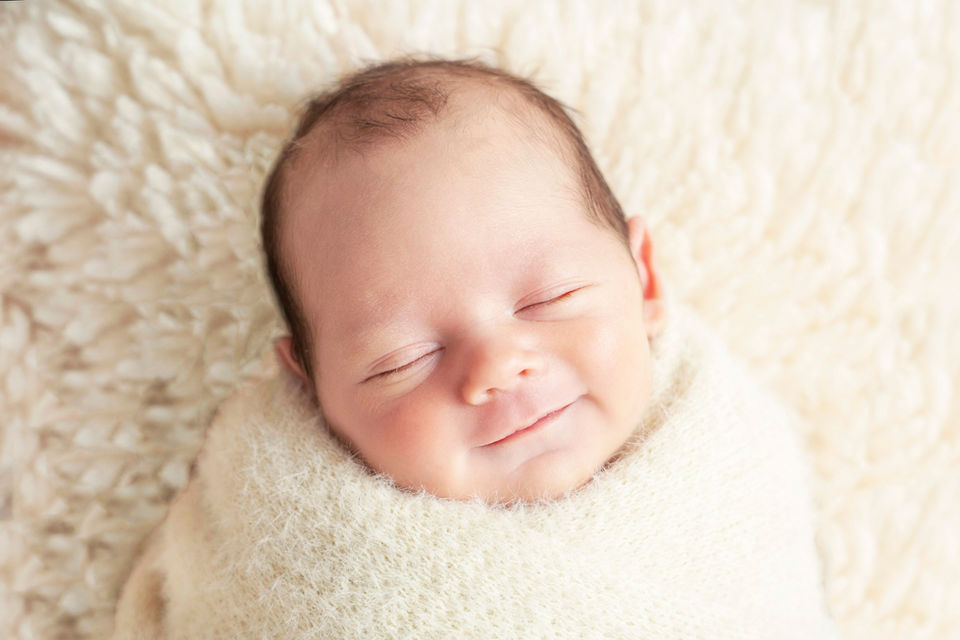 Smiling newborn baby wrapped in a soft cream blanket