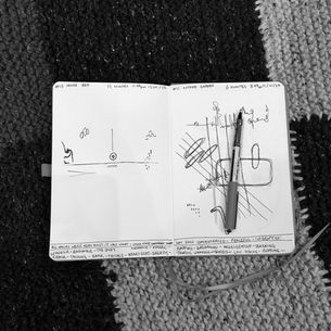 A black and white photo of an open sketchbook with a visual score of mark making on the pages. Each page details the time and place of listening at the top and what was heard and felt along the bottom.